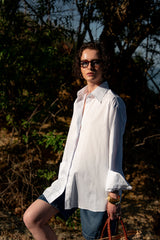Woman wearing a white shirt and sunglasses outdoors with trees in the background