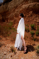 Person wearing a white outfit standing in a natural setting with a red-brown cliff in the background.