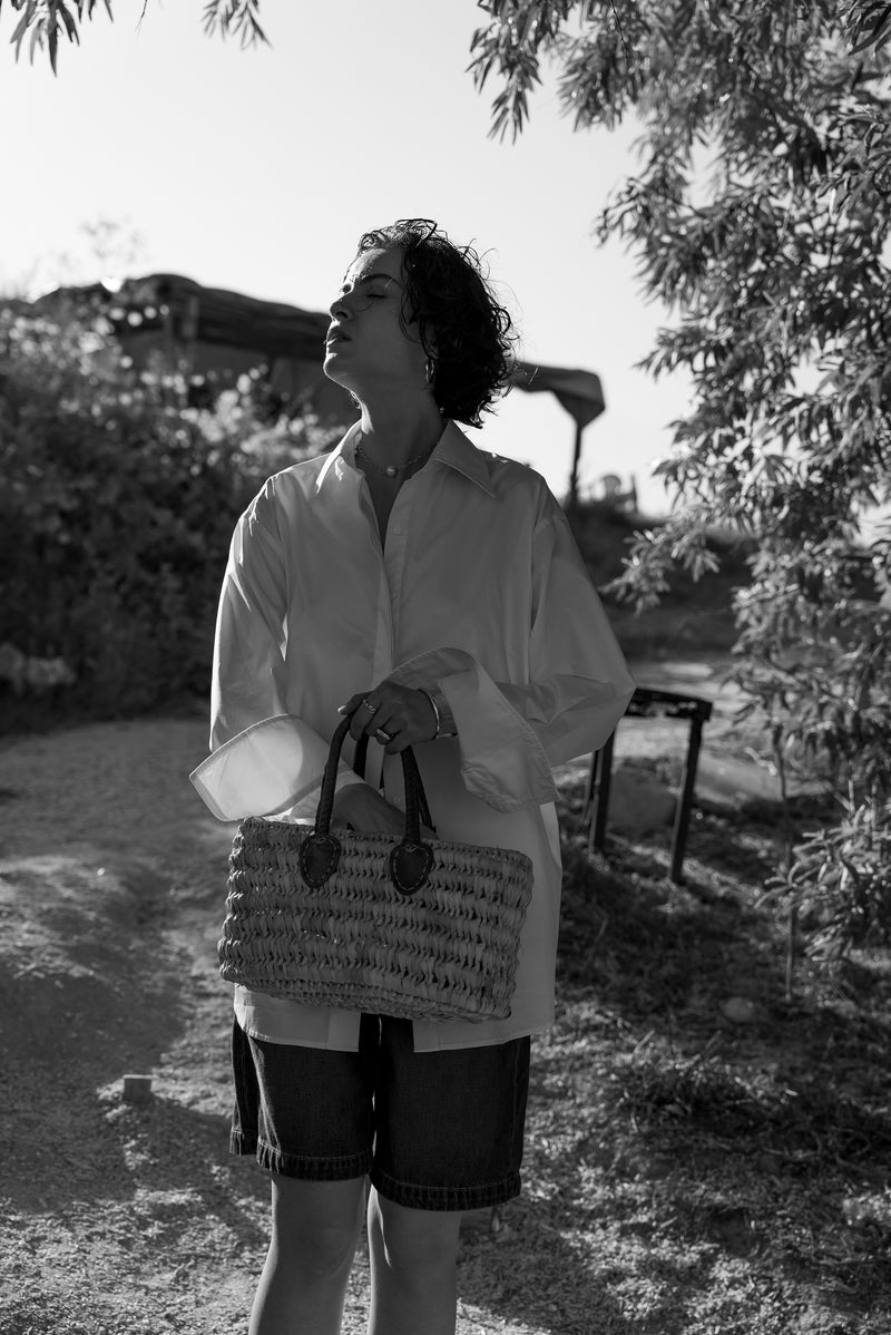 Person holding a bag and a container outdoors with trees and a bench in the background