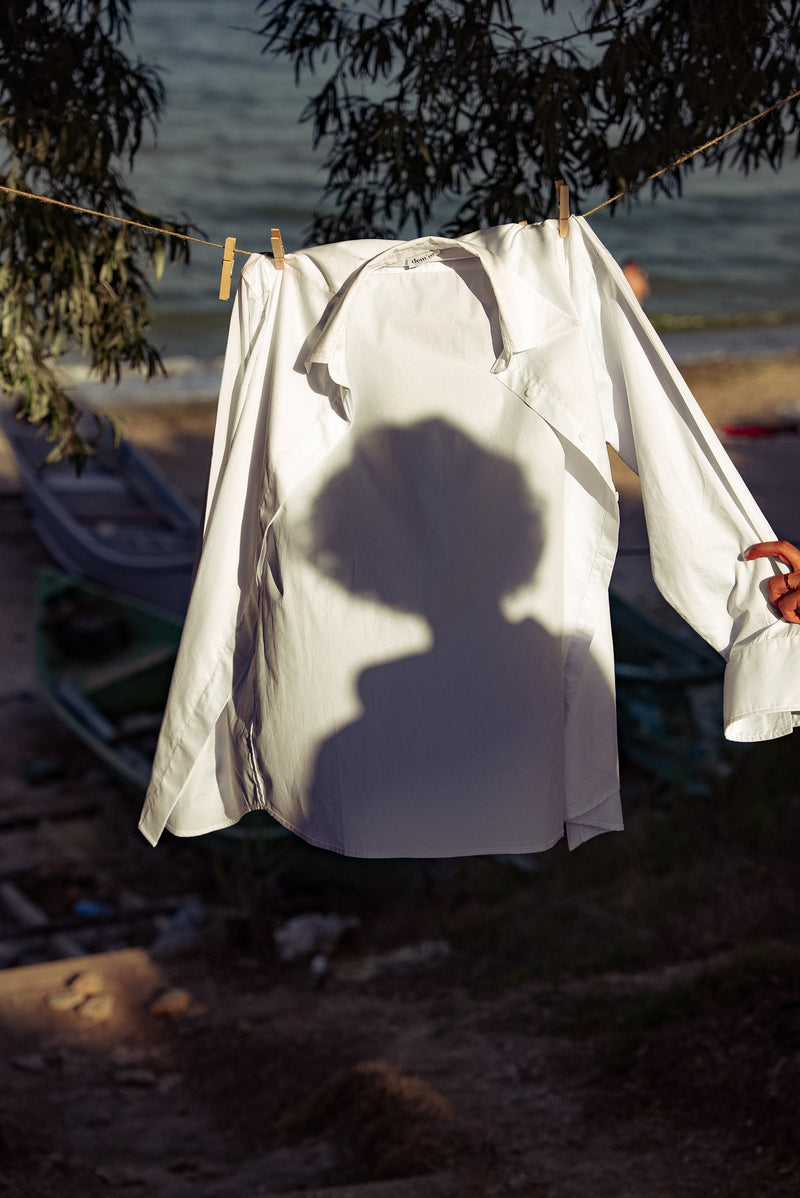 White shirt hanging on a clothesline with a person's shadow cast on it, by water.